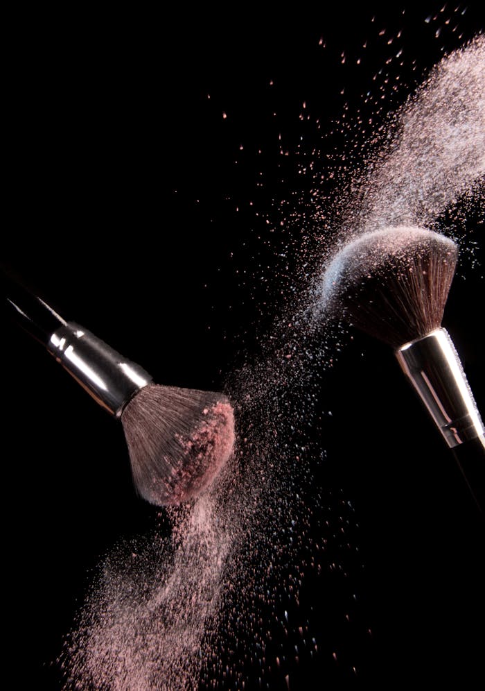 services-02 High-speed capture of makeup brushes dispersing pink powder in motion against a dark background.