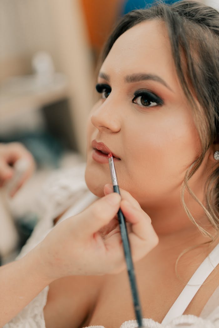 services-03 A makeup artist skillfully applies lipstick to a bride's lips, focusing on detail.