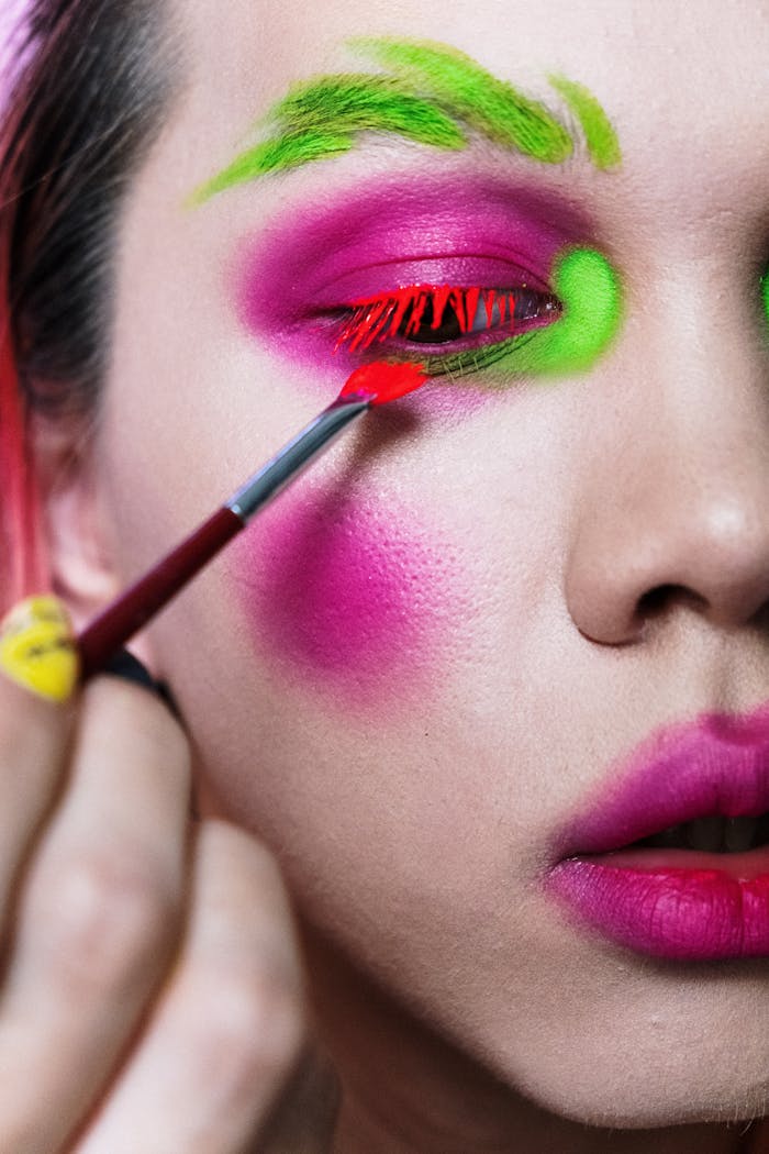 Close-up of an artistic makeup application featuring vivid pink and green colors on a person's face.