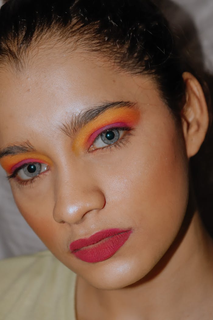 who-we-are Close-up portrait of a woman with vibrant eye makeup and red lipstick, showcasing bold beauty trends.
