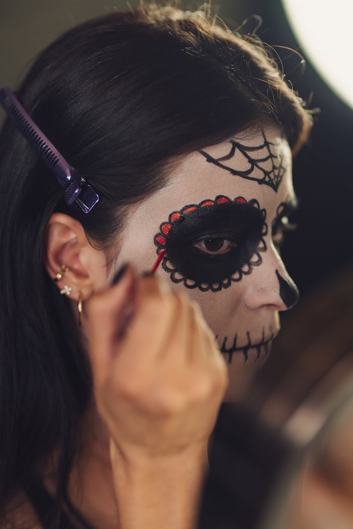 A woman is carefully applying traditional Catrina makeup for Day of the Dead celebrations.
